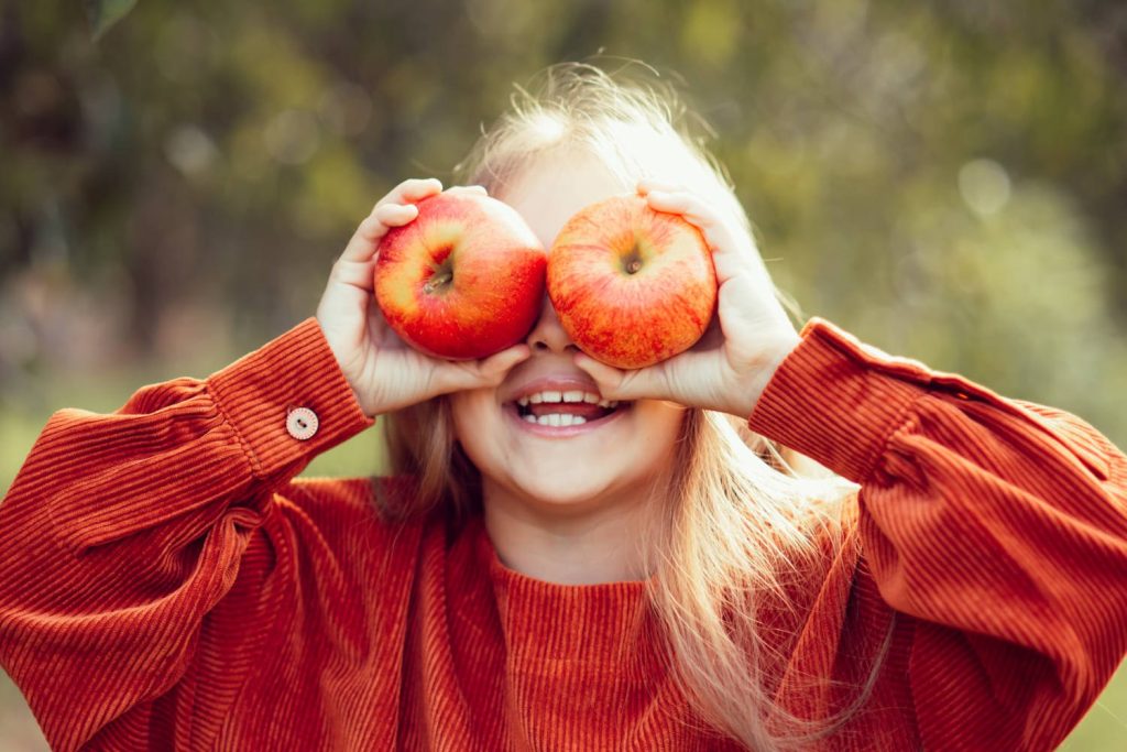 A little girl holding two apples to her eyers