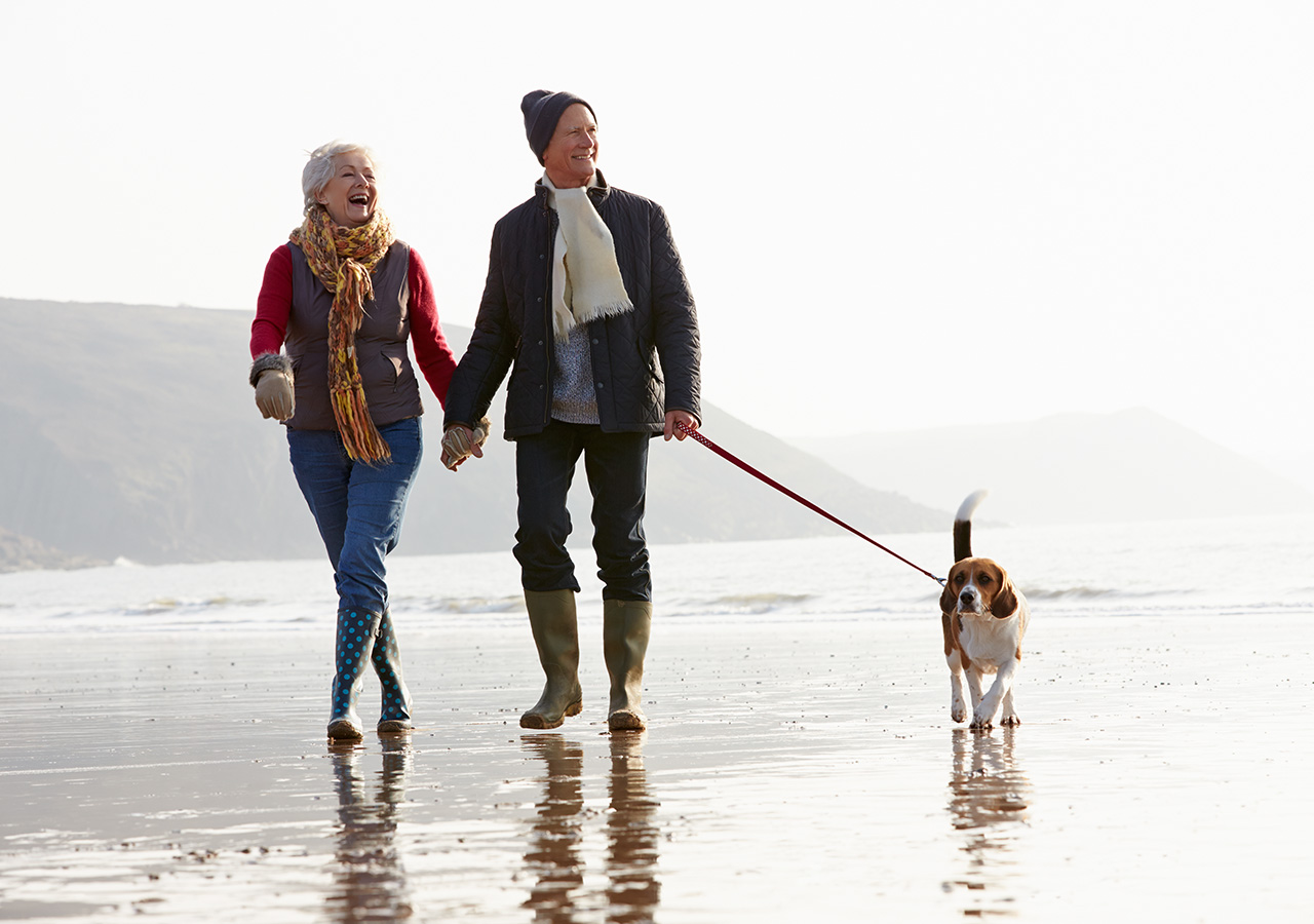 A couple walking their dog on a beach wrapped up in warm clothes