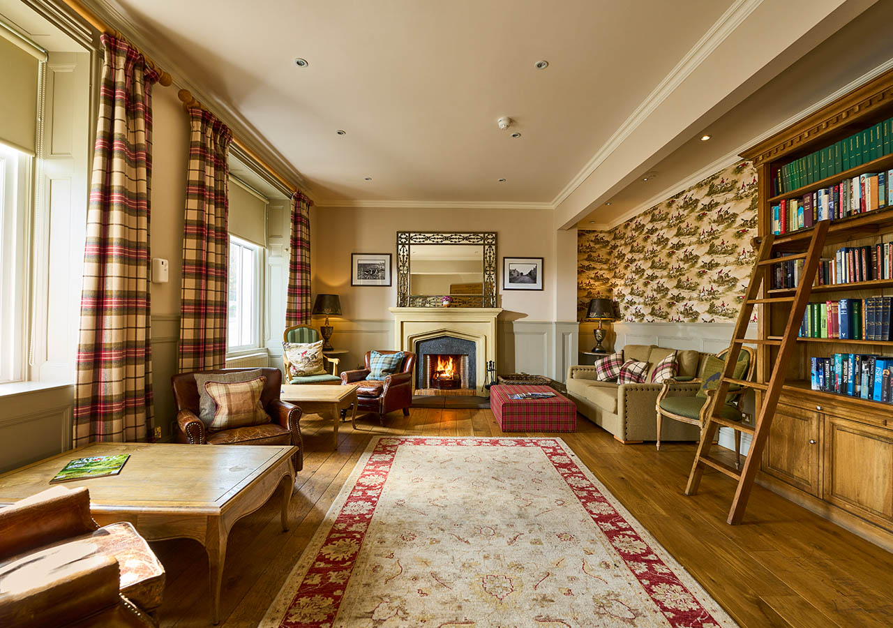 The library with books on shelves, seating and a fireplace at the Ulbster Arms Hotel