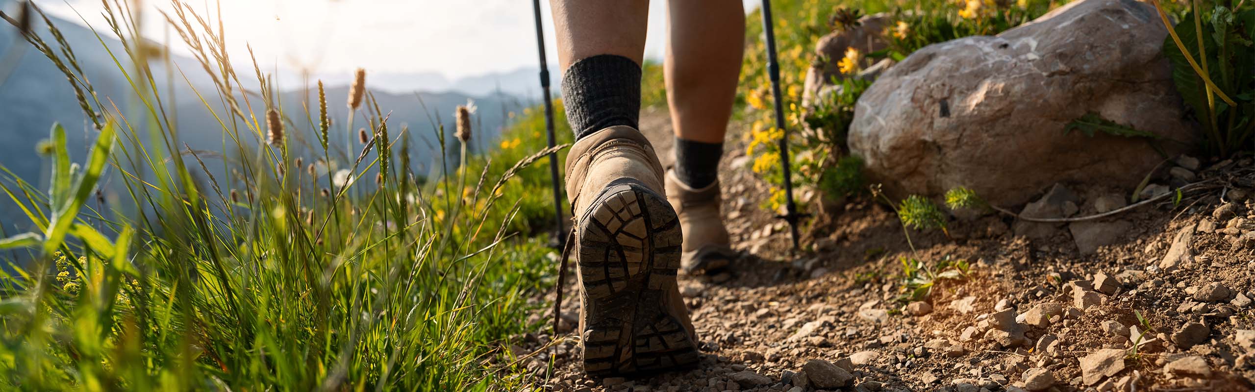 A person in hiking boots with walking sticks walking a trail