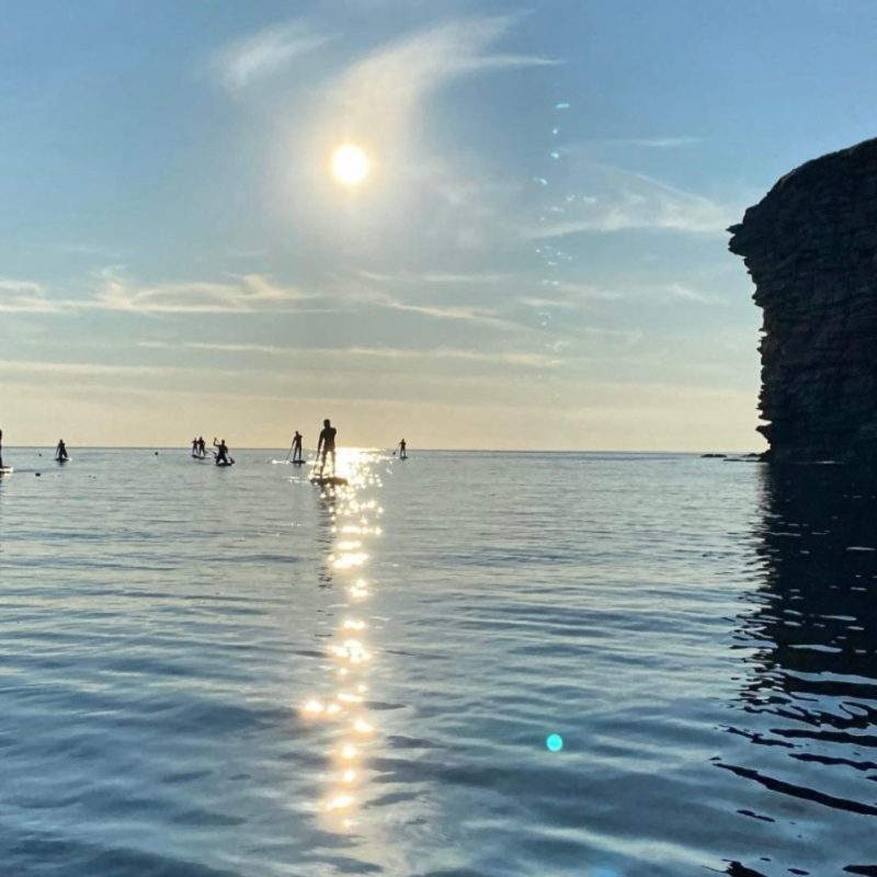 A group paddleboarding in Caithness in the sea by the stacks in summer.