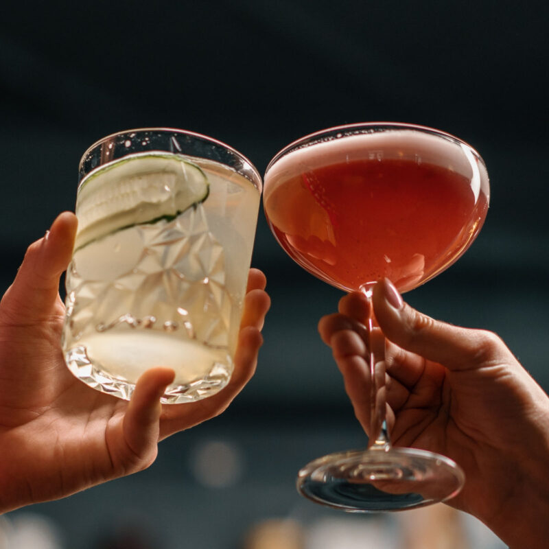 Close up of two people cheering cocktails in bar